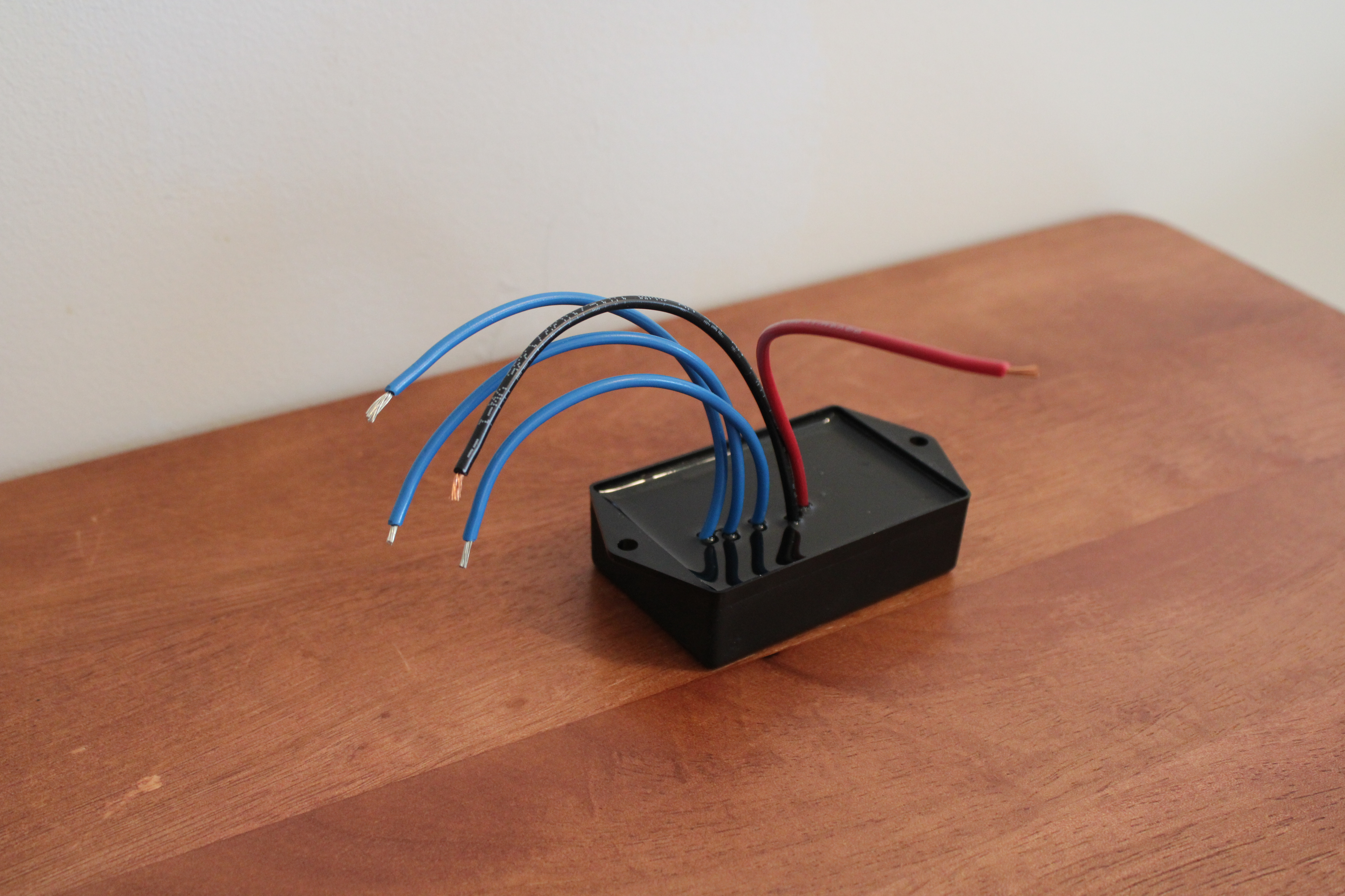 Voltage regulator on a table, small black box with blue and red wires sticking out of it.